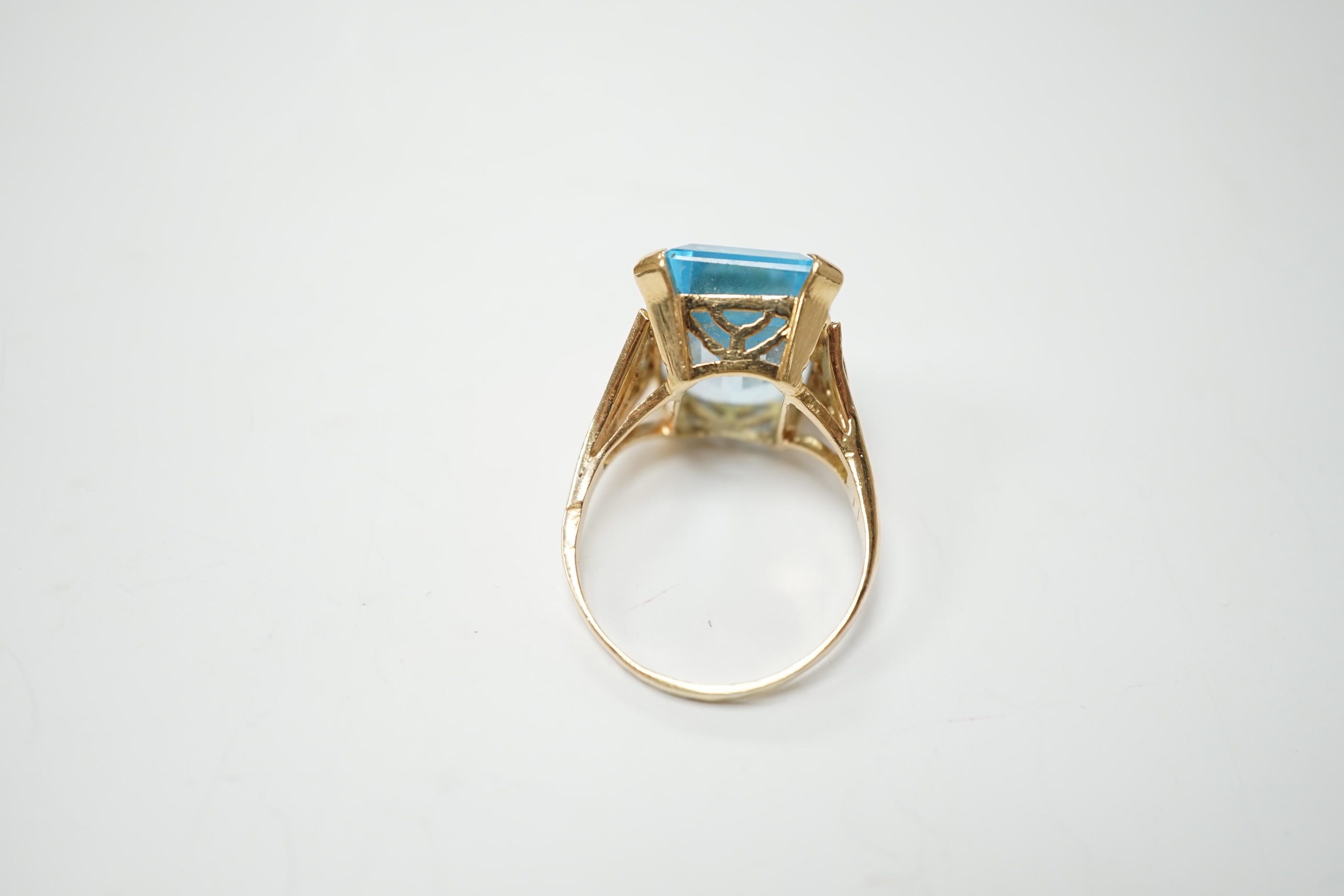 A yellow metal and single stone emerald cut blue topaz set dress ring, with ten stone diamond chip set shoulders, size U/V, gross weight 10.4 grams.